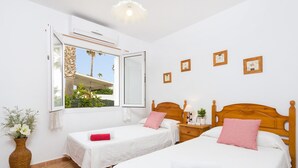 A hotel room with two beds, a window with a view of palm trees, and a wall with framed pictures. - Villa Fernando by Villa Plus (S'Algar)