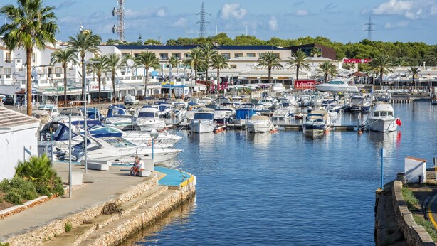 A marina with numerous boats docked, surrounded by buildings and palm trees. - Villa Jessica by Villa Plus (Cap d'Artrutx)