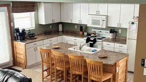A compact kitchen with white cabinets, a microwave, a stove, and a sink. There are three wooden chairs around the island. - Beautiful Townhouse in The Villages of 7 Springs
 (Champion)