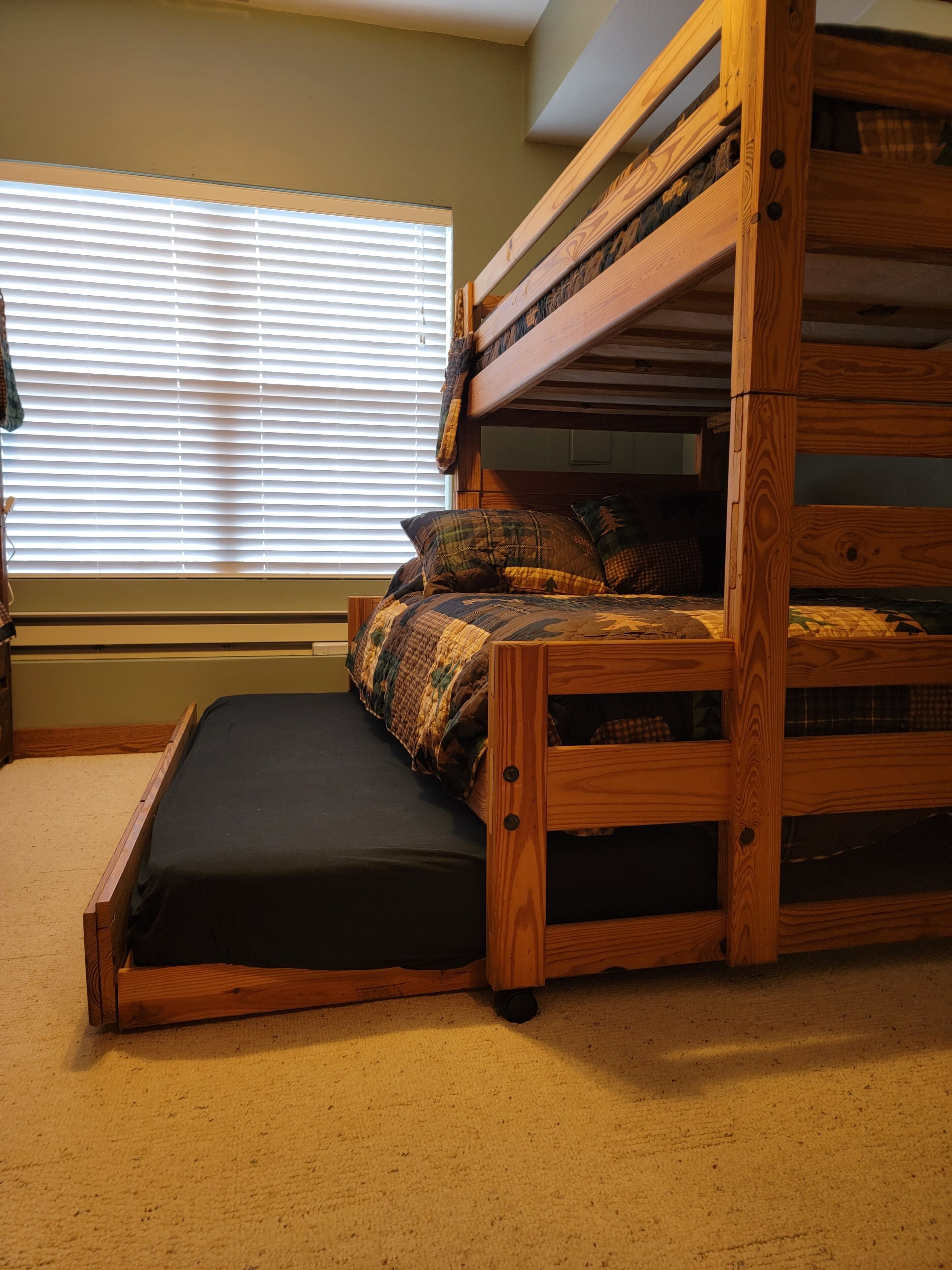A bunk bed with a mattress and pillows, a window with blinds, and a carpeted floor.