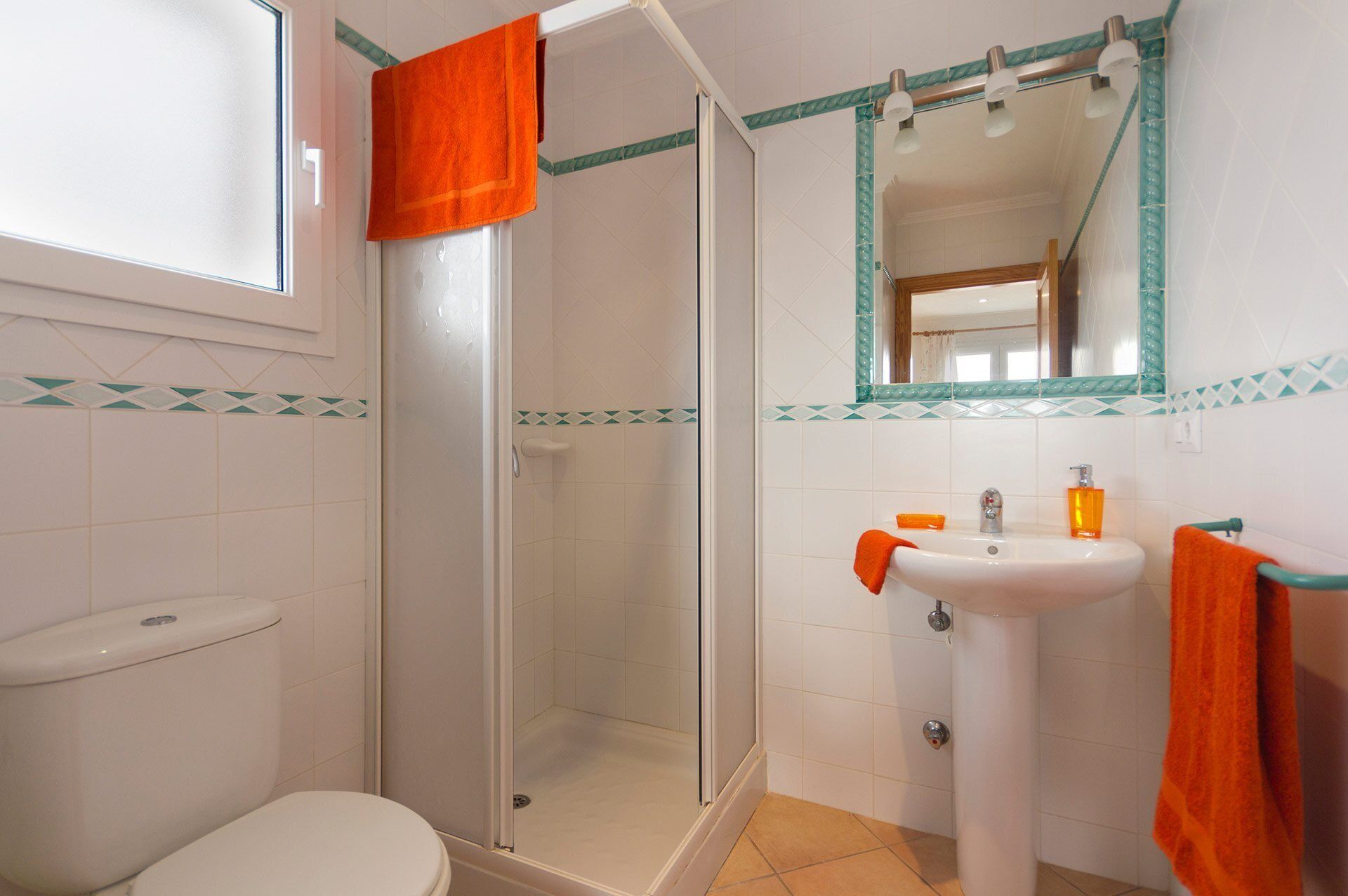 A bathroom with a toilet, shower, sink, and a mirror.