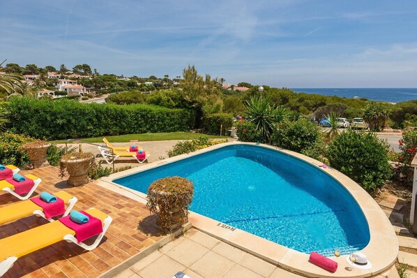 Una piscina con vistas al mar, rodeada de vegetación y algunas tumbonas.