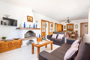 En stue med pejs, sofa, sofabord og spiseområde med træmøbler.