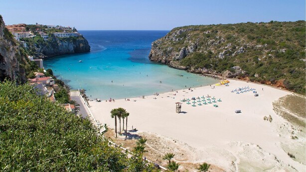 A coastal beach with clear blue waters, a sandy shore, and a rocky hillside. - Villa Mirador by Villa Plus (Cala en Porter)