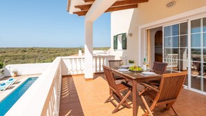A terrace with a pool, wooden furniture, and a view of the landscape. - Villa Mirador by Villa Plus (Cala en Porter)