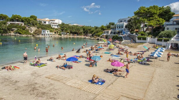 Una playa con gente tomando el sol y nadando, rodeada de edificios y árboles.