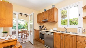 A modern kitchen with wooden cabinets, a stainless steel dishwasher, and a window overlooking greenery.