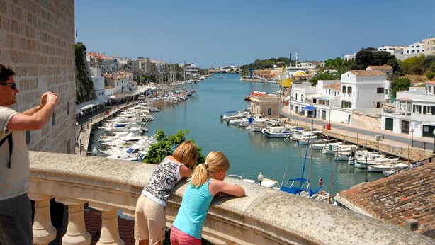 A coastal town with a marina filled with boats, white buildings, and a clear blue sky.