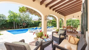 A covered outdoor area with a pool, lounge chairs, and wicker furniture.