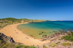 Una playa con aguas turquesas cristalinas, orilla arenosa y afloramientos rocosos.