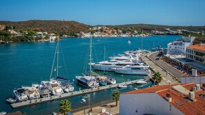 En lysthavn med flere sejlbåde i havnen, en kystby i baggrunden, og en markant hvid bygning med skiltet "Il Porto".