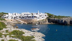 Uma vila costeira com edifícios brancos, linha costeira rochosa e um barco atracado perto da água.