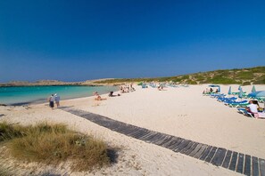 A beach with a paved walkway, beach chairs, and umbrellas.
