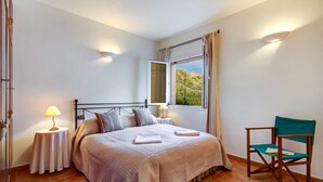 Quarto com cama, mesas de cabeceira, uma cadeira e janela com cortinas.