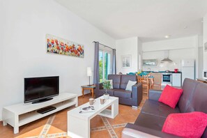 Ett modernt vardagsrum med en platt-TV, en soffa, ett soffbord och en matplats med ett bord och stolar.