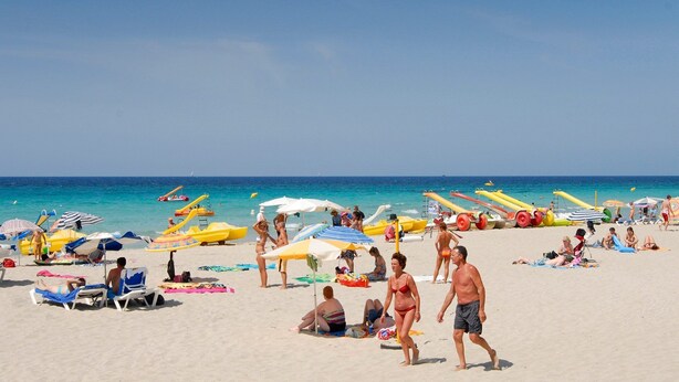A beach with people sunbathing, umbrellas, and boats. - Villa Torrenit by Villa Plus (Alayor)