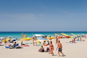En strand med folk som solar, parasoller och båtar.