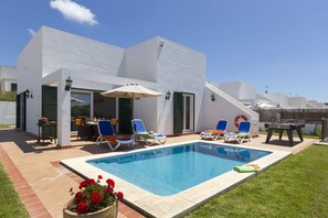 A modern outdoor pool area with lounge chairs, a barbecue setup, and a small table. - Villa Torrenit by Villa Plus (Alayor)