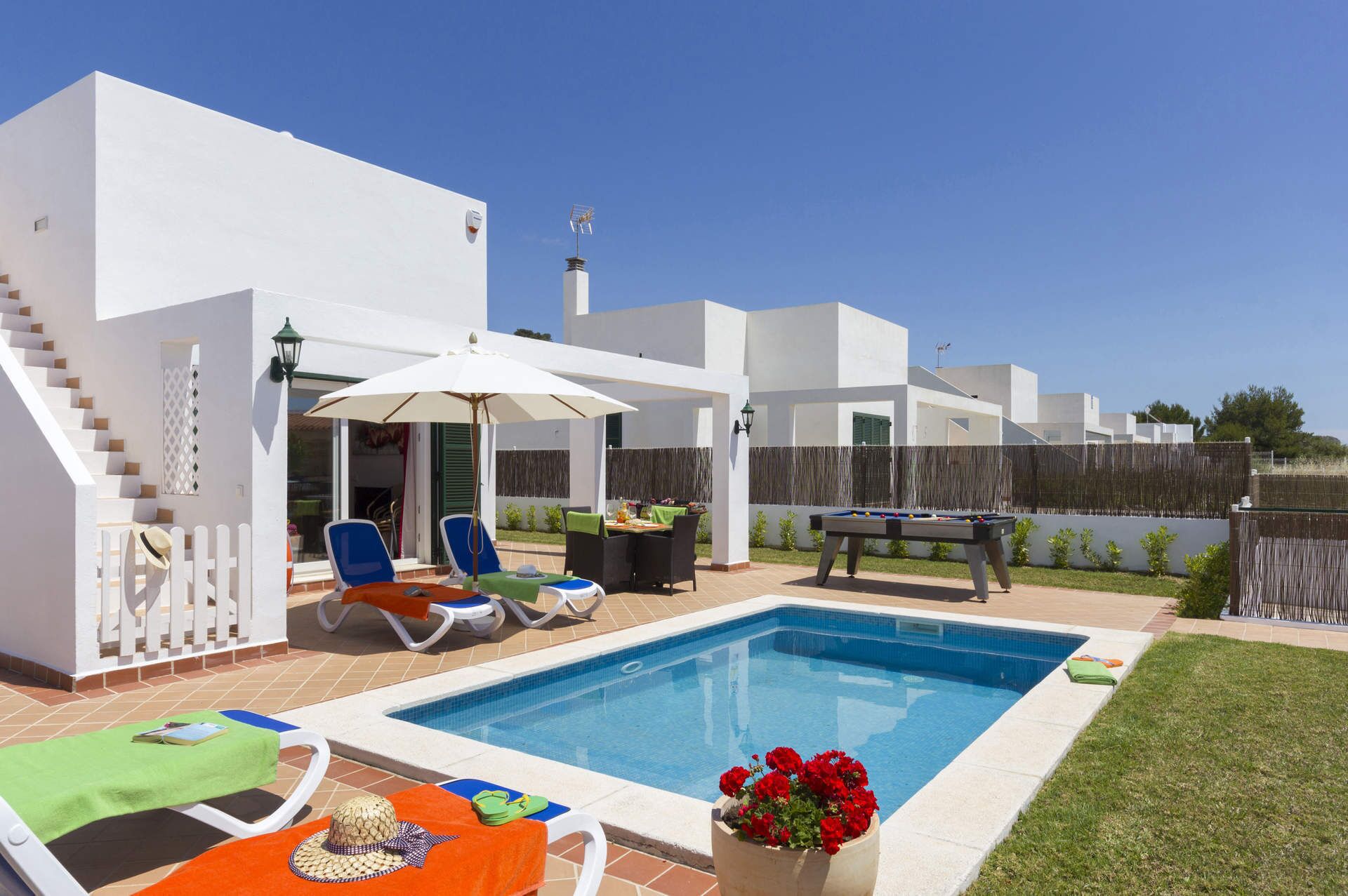 A pool area with lounge chairs, a table with a green umbrella, and a pool table.