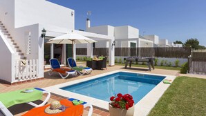 A pool area with lounge chairs, a table with a green umbrella, and a pool table. - Villa Torresoli by Villa Plus (Alayor)