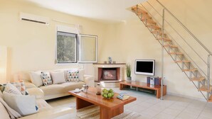 Ein Wohnzimmer mit Sofa, Couchtisch, Kamin, Fernseher und einer Treppe.