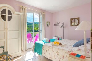 A bedroom with a bed, a window with curtains, a chair, a bedside table, and a lamp.