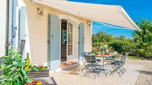 Eine Terrasse mit Tisch und Stühlen, einem Grill und einem überdachten Bereich mit Blick auf den Garten.