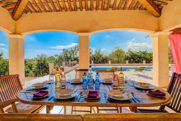 An outdoor dining area with a view of a pool and trees.