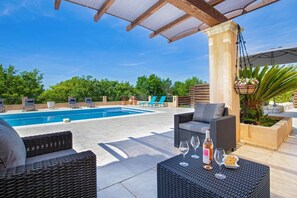 A rooftop pool with lounge chairs, a wicker table with wine glasses, and a hanging planter.