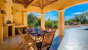 An outdoor patio with a dining table, chairs, and a grill. - Villa Soleiade by Villa Plus (Saint-Cézaire-sur-Siagne)