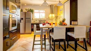 A modern kitchen with stainless steel appliances, a dining area with bar stools, and a window providing natural light. - Villa Soleiade by Villa Plus (Saint-Cézaire-sur-Siagne)