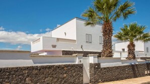 Una villa bianca con un muro in pietra, palme e un cielo azzurro limpido.
