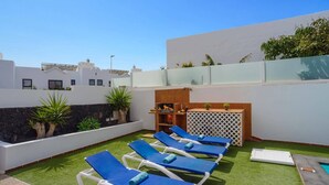 Una terrazza sul tetto con poltrone da relax blu, un'area barbecue e vista sugli edifici circostanti.