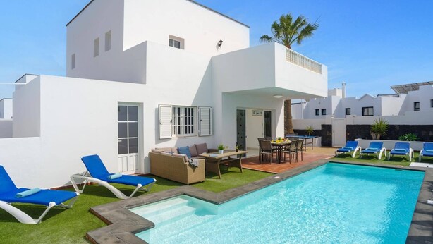 Una villa bianca moderna con piscina, area salotto esterna e patio.