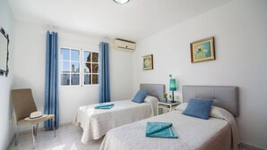 Une chambre d’hôtel avec deux lits, une chaise, une fenêtre avec des rideaux et deux tableaux encadrés accrochés au mur.