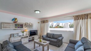 Ein Wohnzimmer mit grauen Sofas, einem Couchtisch, einem Fernseher und einem Fenster mit Vorhängen.