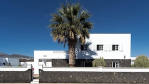 Ein modernes, weißes Gebäude mit einer Steinmauer, einer Palme und blauem Himmel.