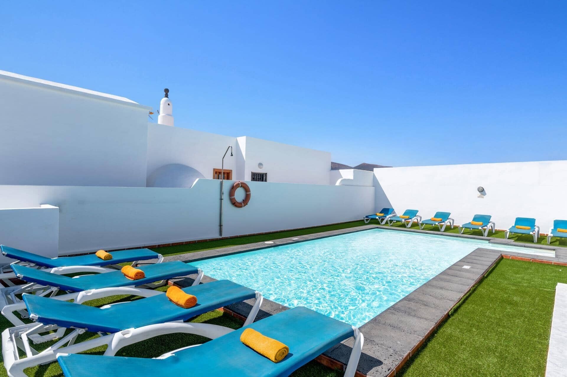 Zona de piscina con sillas reclinables azules y un flotador en la pared.