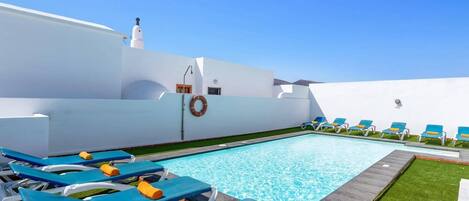 Zona de piscina con sillas reclinables azules y un flotador en la pared.