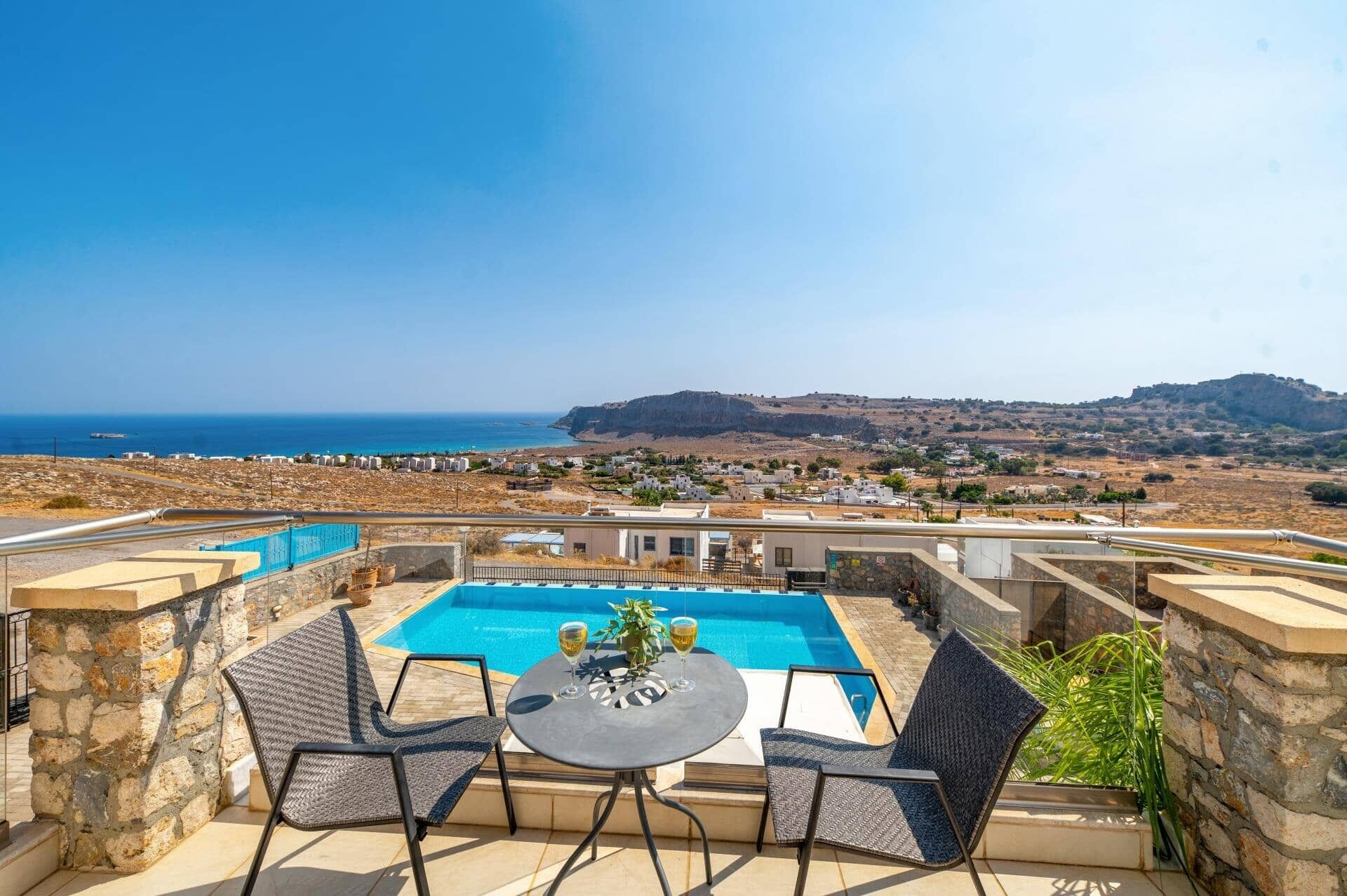 Piscina en la azotea con dos sillas y una mesa, con vistas a un pueblo costero y al mar.