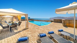 Ein Poolbereich auf dem Dach mit freiem Blick auf das Meer, Liegestühle und eine überdachte Sitzgruppe.