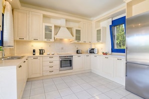 A modern kitchen with white cabinetry, a stainless steel refrigerator, a built-in oven, and a window with a blue frame.