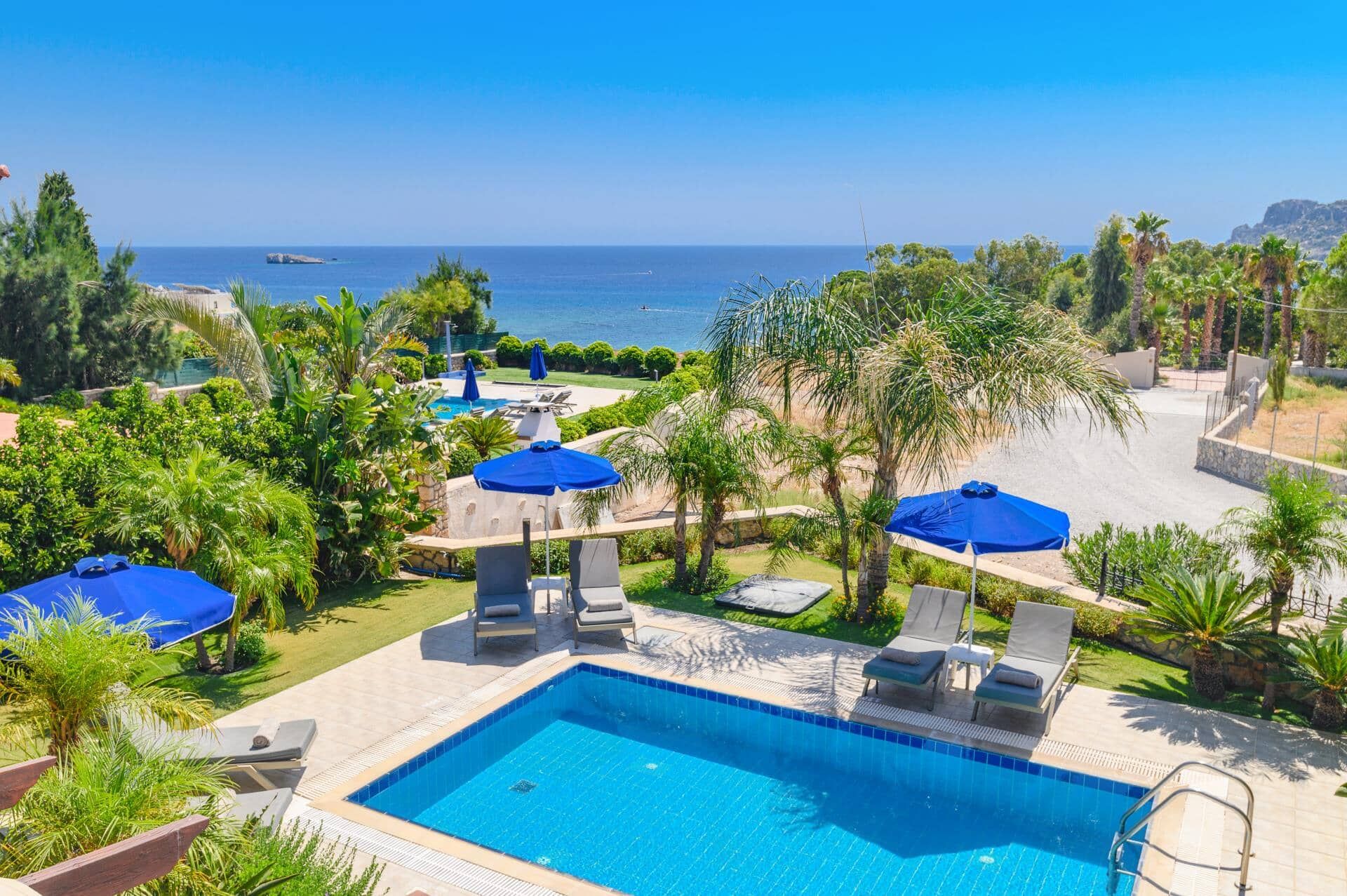 A pool area with a view of the sea, surrounded by palm trees and lounge chairs.