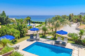 A pool area with a view of the sea, surrounded by palm trees and lounge chairs.