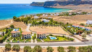 Vista aérea de uma área residencial costeira com villas, uma piscina e vista clara para o mar.