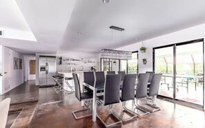 A modern kitchen with a dining area, large windows, and a view of the outdoors.