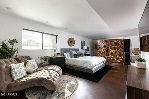 A modern bedroom with a large bed, a sofa, a desk, and a decorative wall panel.