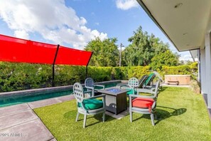 A patio area with a pool, outdoor furniture, and a red canopy.