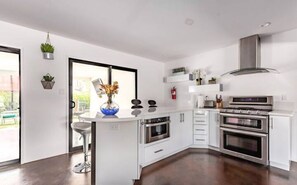 A modern kitchen with white cabinetry, a central island with bar stools, a stainless steel range hood, and double ovens. - Designer 5 Bd Home/Fountain Pool/ Spa/ Game Patio (Phoenix)