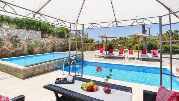 A covered outdoor pool area with lounge chairs and a table with fruit and drinks. - Villa Despina by Villa Plus (Pefki)